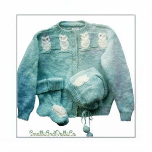 May include: A light blue, variegated knit cardigan featuring a row of four white owl appliques across the chest, paired with matching knit socks and a bonnet with a white owl applique and dangling pom-poms. The text SmallsAndDollsCo is visible.