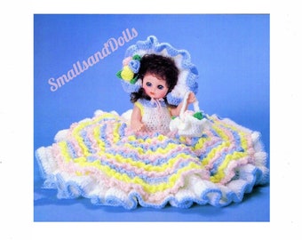 May include: A crocheted doll dress with a white, yellow, pink, and blue color scheme. The dress has a ruffled skirt and is worn by a doll with brown hair and blue eyes. The doll is wearing a matching crocheted hat with a flower.