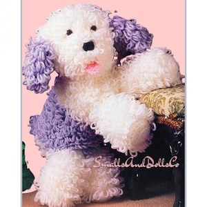 May include: A plush dog toy crafted from white and lavender looped yarn, featuring a black nose, dark eyes, and a small pink tongue. The text SmallsAndDollsCo is printed in a cursive font near the base of the stuffed animal figure.
