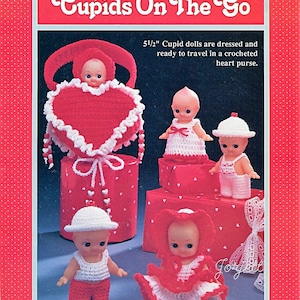 Könnte beinhalten: Vintage-Bild mit 14 cm großen Amor-Puppen in gehäkelten Outfits und Hüten. Eine Puppe befindet sich in einer roten herzförmigen Tasche. Die Puppen stehen auf roten Schachteln mit weißen Herzmustern. Der Text "Cupids On The Go" steht oben.