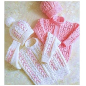 Pode incluir: Dois casacos de malha para bebé com chapéus a condizer. Um casaco é branco com detalhes cor-de-rosa, e o outro é cor-de-rosa com detalhes brancos. Ambos os casacos têm um padrão de malha de cabo.