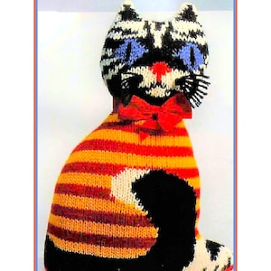 Puede incluir: Un juguete de gato tejido con rayas negras, blancas, naranjas y rojas. El gato tiene ojos azules y un lazo rojo.