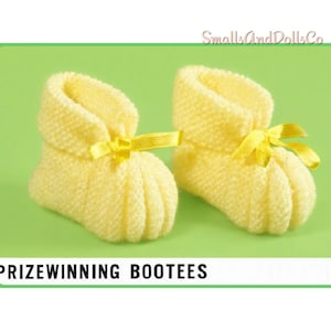 May include: A pair of pale yellow knitted bootees featuring a ribbed texture and a matching yellow satin ribbon bow tied at the front. The text SmallsAndDollsCo and PRIZEWINNING BOOTEES are visible on the image.