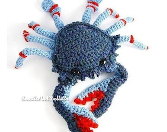 Puede incluir: Un cangrejo azul de crochet con detalles rojos. El cangrejo tiene un cuerpo texturizado y garras detalladas.