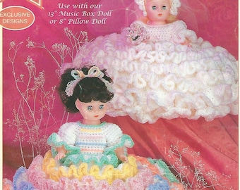 May include: Two crocheted doll dresses, one white and one with rainbow colored ruffles. The text "Crochet a Lovely Bridal Gown or Rainbow Party Dress" is visible. "Use with our 13" Music Box Doll or 8" Pillow Doll" is also visible.