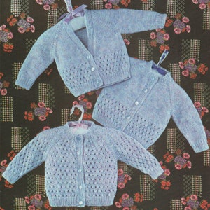 May include: Two light blue knitted baby cardigans with button fastenings. One cardigan has a V-neck and the other has a round neck.