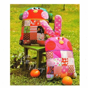 May include: Two patchwork fabric toys, one red and one pink, with smiling faces and googly eyes. The toys are sitting on a green wooden stool in a grassy area. The text "Best Patterns Palooza" is visible in the image.