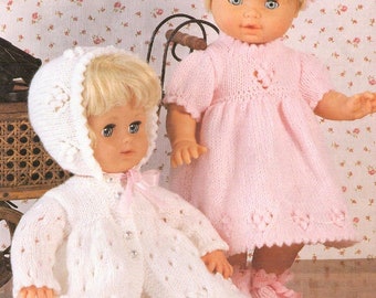 May include: Two knitted doll outfits, one white with a hood and the other pink with a headband. Both outfits feature delicate lace details and are perfect for a baby doll.