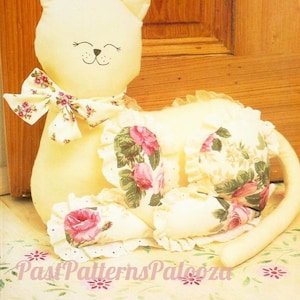 May include: A white stuffed cat doorstop with a floral print and a bow. The cat is sitting on a light yellow surface with a floral pattern.