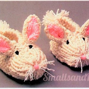 May include: A pair of knitted bunny slippers in white with pink ears and white whiskers. The slippers are made with a soft, fluffy yarn.