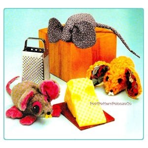 May include: A whimsical still life featuring plush toy mice, a cheese grater, and a wedge of cheese. The mice are in various colors and patterns, with one atop a wooden box. The cheese is yellow, and the grater is silver.