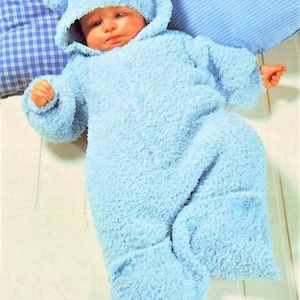 May include: A light blue knitted baby sleepsuit with a hood and bear ears. The sleepsuit has buttons down the front and is made of a soft, fluffy yarn.