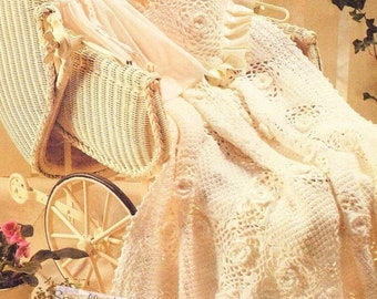 May include: A white crocheted baby blanket with a delicate floral pattern. The blanket is draped over a white wicker baby carriage with a doll inside. The image includes the text "Smalls And Dolls".