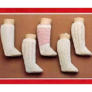 Könnte beinhalten: Fünf Paar gestrickte Puppensocken in Weiß und Rosa. Die Socken werden auf einer braunen Oberfläche präsentiert.