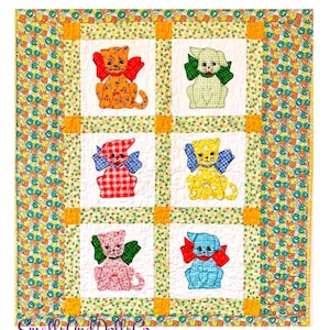May include: A quilt with a white background and a patchwork design featuring six colorful cats with bows. The cats are in a grid pattern with a yellow and green border. The quilt is labeled "Smalls and Dolls Co."