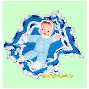 May include: A doll with light skin and brown hair wearing a light blue crocheted outfit with a matching bonnet, booties, and mittens. The doll is resting on a crocheted blanket featuring a pattern of white, light blue, and dark blue stripes.