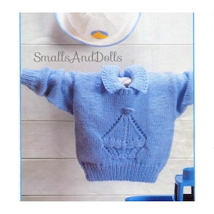 May include: A light blue knitted jumper with a sailboat design on the front. The jumper has a collar and long sleeves. "SmallsAndDolls" is written on the top of the image.