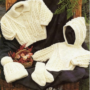May include: A set of knitted baby clothes in a cream color, including a cardigan, a hooded sweater, a hat, and a pair of mittens.