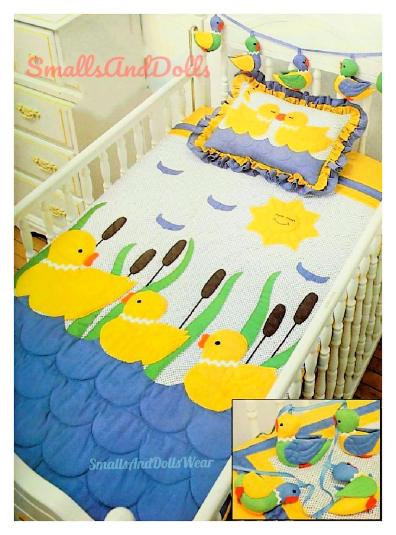 May include: A white crib with a blue and yellow baby quilt featuring a sun, ducks, and cattails. The quilt is made with a white background and has a blue border. The crib is decorated with a yellow and blue pillow and a garland of colorful birds.