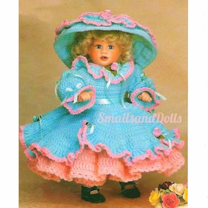 Könnte beinhalten: Ein gehäkeltes Puppenkleid in hellblau mit rosa Besatz und einer passenden Mütze. Das Kleid hat einen Rüschenrock und eine Schleife. Die Puppe trägt schwarze Schuhe.