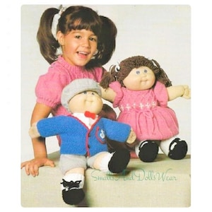 May include: A young girl is playing with two Cabbage Patch Kids dolls. One doll is wearing a pink dress and the other is wearing a blue sweater and grey trousers. The dolls are sitting on a white surface. The text "Smalls and Dolls Wear" is visible in the bottom right corner of the image.