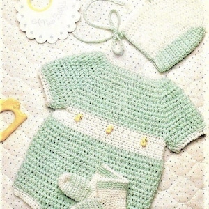 May include: A crocheted baby outfit in green and white with yellow buttons. The outfit includes a onesie, a hat, and booties.