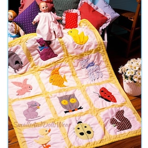 May include: A white baby quilt with a yellow border featuring twelve square patches, each displaying a different fabric appliqué animal or insect, including a chick, cat, fish, lamb, rabbit, owl, butterfly, mouse, ladybug, and squirrel, with the text SmallsAndDollsWear.