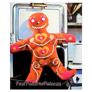 May include: A gingerbread man doll with a smiling face, orange body, and pink and yellow accents. The doll is standing in front of a vintage stove.