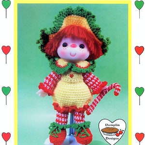 May include: A crochet doll named Peppermint Stick, with a yellow dress, red and white patterned sleeves and legs, and a green and yellow hat. The doll holds a candy cane and has a heart-shaped logo. Text reads "Peppermint Stick" and "Brought to you directly from 'Lollipop Lane'".