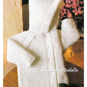 May include: A white, knitted baby jacket with a hood. The jacket has a textured stitch pattern, long sleeves, and three white buttons down the front. The text "SmallsAndDollsCo" is visible on the front of the jacket.