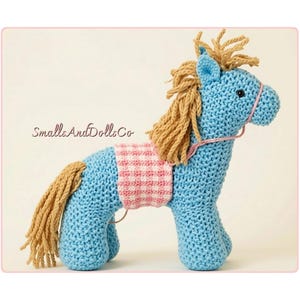 May include: A light blue crocheted horse toy with a tan yarn mane and tail, featuring a pink and white gingham patterned saddle blanket and a thin pink bridle. The text SmallsAndDollsCo is visible in the center left of the image.