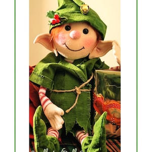 Peut inclure: Une poupée elfe en tissu avec des cheveux orange, des joues roses et de grandes oreilles pointues. La poupée porte un chapeau vert avec une clochette dorée et du houx, une tunique verte avec une ceinture en ficelle, et des collants rayés.