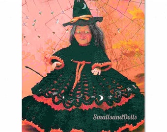 Könnte beinhalten: Häkelpuppe einer Hexe, die ein schwarzes Kleid mit orangefarbenem Besatz, einen schwarzen Hexenhut mit gelbem Band und silberne Halbmond- und Sternverzierungen trägt. Die Puppe steht auf einem rosa und orangefarbenen Hintergrund mit einem Spinnennetz-Muster.