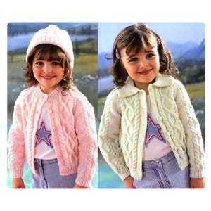 May include: Two children wearing colorful knitted cardigans with cable knit patterns. The cardigan on the left is pink and the cardigan on the right is light green.