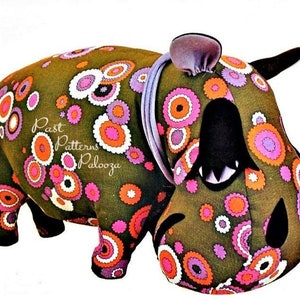 May include: A plush green hippopotamus toy with a purple headband and black eyes. The hippopotamus is covered in a pattern of pink, white, and orange circles. The text "Past Patterns Palooza" is printed on the hippopotamus's side.