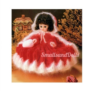 May include: A doll wearing a red and white crocheted dress and hood. The dress has a fluffy, textured appearance with a scalloped white trim. The doll has dark curly hair and is set against a backdrop with the text "SmallsandDolls".
