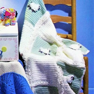 May include: A handmade crochet baby blanket in shades of white and mint green, adorned with sheep appliqués. The blanket is draped over a wooden chair in a nursery setting. The text "SmallsandDolls" is visible.