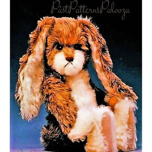 Könnte beinhalten: Ein braunes und weißes Plüschkaninchen mit langen, schlaffen Ohren. Das Kaninchen sitzt mit gekreuzten Pfoten und hat einen traurigen Gesichtsausdruck. Der Hintergrund ist hellblau.