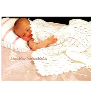 May include: A white crocheted baby blanket with a diamond pattern. The blanket is draped over a sleeping baby on a pink surface.