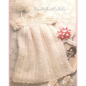 May include: A white crocheted baby dress with a matching bonnet and booties. The dress has a scalloped hem and a satin ribbon tied at the waist. The set is perfect for a christening or special occasion.