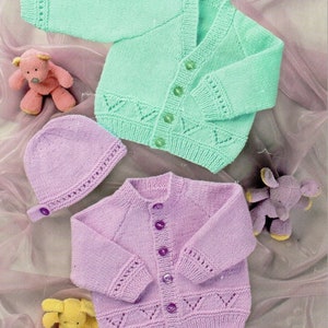 Könnte beinhalten: Zwei gestrickte Baby-Cardigans, einer in Hellgrün und einer in Lavendel, mit passenden Knöpfen. Die Cardigans haben ein zartes Spitzenmuster an den Rändern und ein schlichtes, klassisches Design.