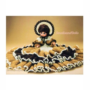 May include: Crochet doll pattern featuring a doll wearing a brown and white dress with a brown and white hat. The doll is sitting on a brown and white crocheted skirt. The pattern is called "Smalls and Dolls".
