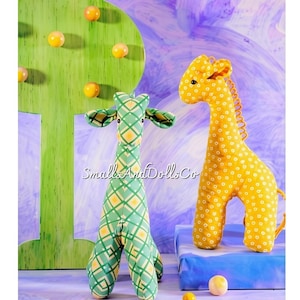 May include: Two stuffed giraffe toys with the text SmallsAndDollsCo. One giraffe is green with a yellow diamond grid pattern, and the other is yellow with a white floral pattern. Both have long necks, small ears, and a soft fabric construction.