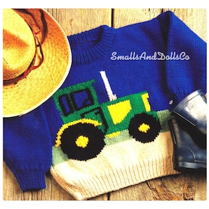 May include: Blue knitted jumper with a green tractor design. The jumper has a white and green trim around the neck and sleeves. The text "SmallsAndDollsCo" is printed on the jumper.