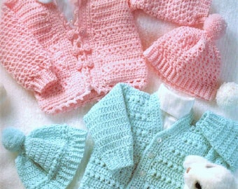 May include: Two crocheted baby cardigan sweaters and hats. One set is pink and the other is light blue. Both sets have a button closure and a pom-pom on the hat.