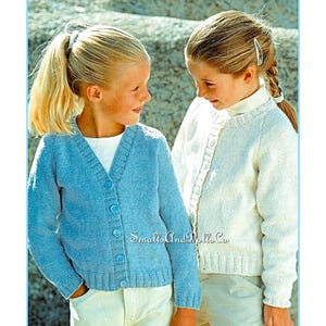 以下が含まれることがあります： 2人の女の子がニットのカーディガンを着ています。左側の女の子はボタン付きの薄いブルーのカーディガンを着ています。右側の女の子はボタン付きの白いカーディガンを着ています。両方のカーディガンはVネックです。