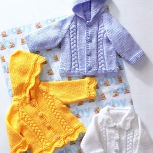 Op de afbeelding: Drie gebreide babyjasjes in verschillende kleuren: lavendel, geel en wit. Elk jasje heeft een capuchon, knoopsluiting en een kabelbreipatroon.