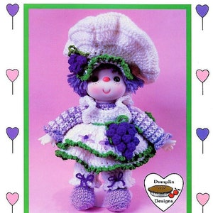May include: A crocheted doll wearing a white hat, purple dress, and green shoes. The doll is holding a bunch of purple grapes. The doll is called "Grape Jelly" and is from "Lollipop Lane".