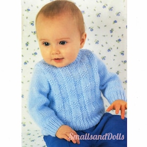 Könnte beinhalten: Ein hellblauer gestrickter Baby-Pullover mit Zopfmuster. Der Pullover wird von einem Baby getragen, das auf einem floral gemusterten Hintergrund sitzt.