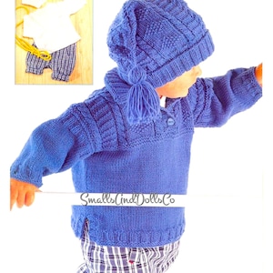 May include: A blue knitted sweater with a cable knit pattern and a matching blue hat with a pom-pom. The sweater has a high collar and a button closure. The hat is pulled down over the child's ears. "Smalls and Dolls Co." is printed on the sweater.